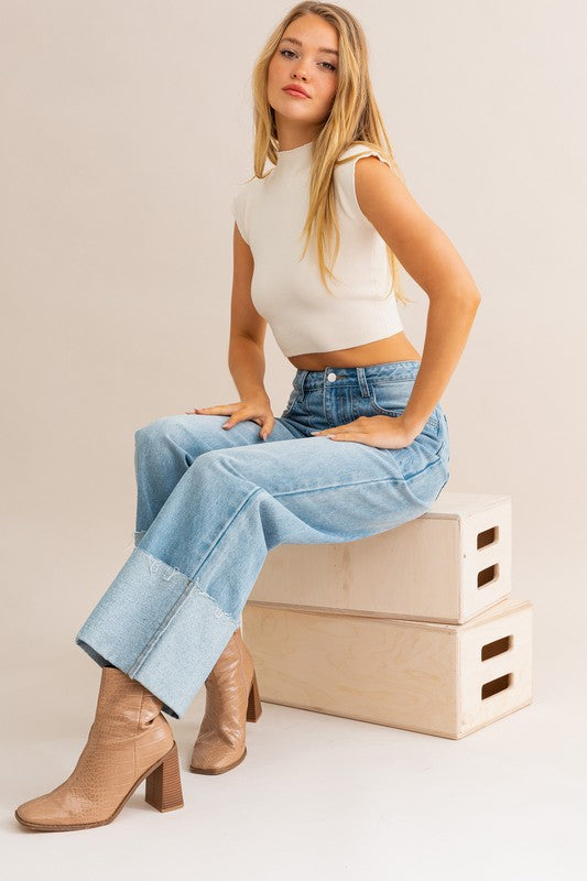 High-waisted wide leg cuffed jeans worn by a model sitting on wooden boxes.